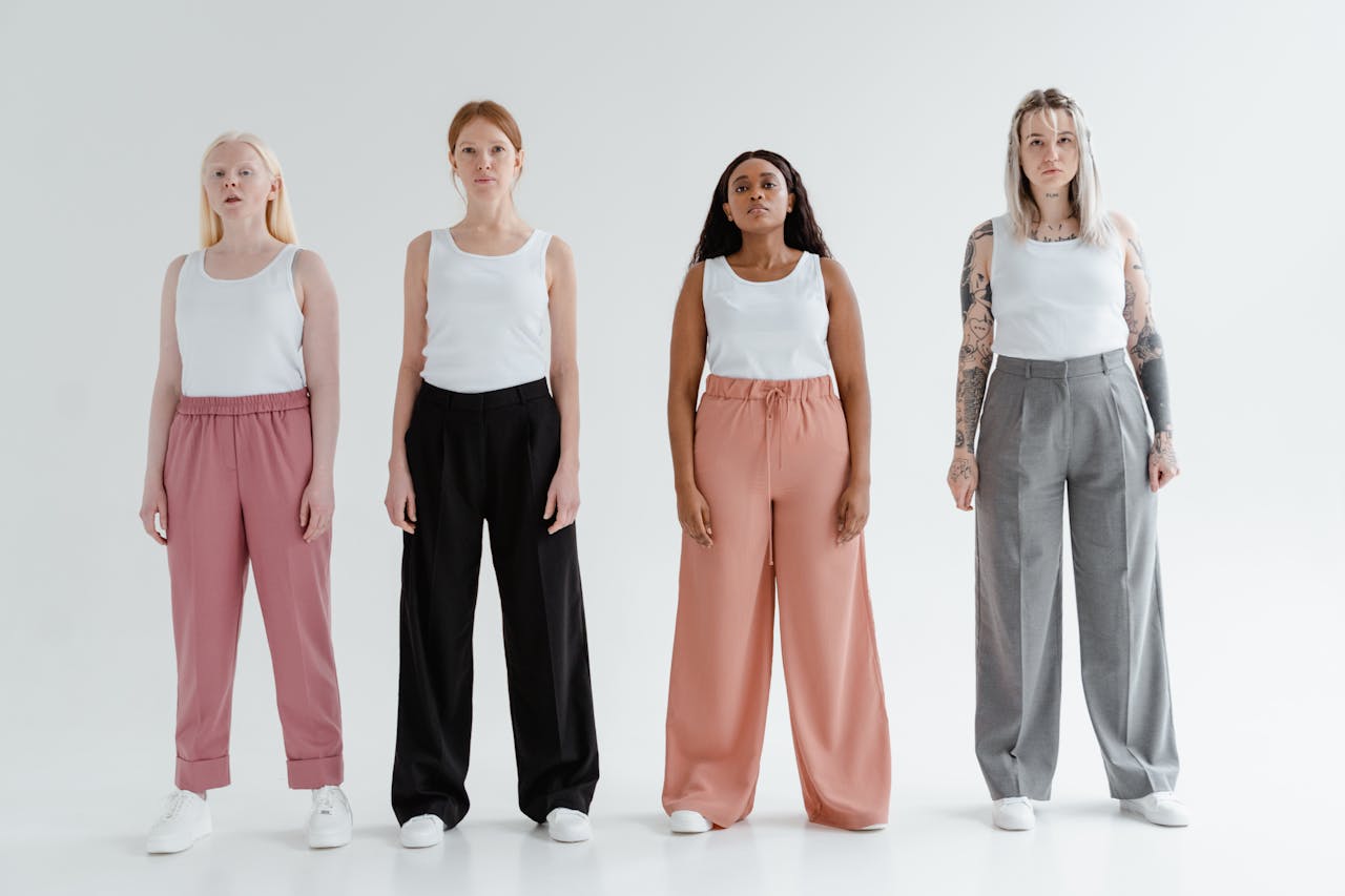 our-experience Four diverse women stand confidently in stylish pants and white tank tops against a white backdrop.